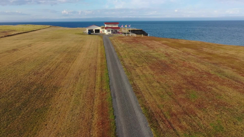 Drone shot over the long driveway leading to a residential home with patriotic flags on the rugged coast of Caraquet, Canada. Calm sea in background. Royalty-Free Stock Footage #1091797787