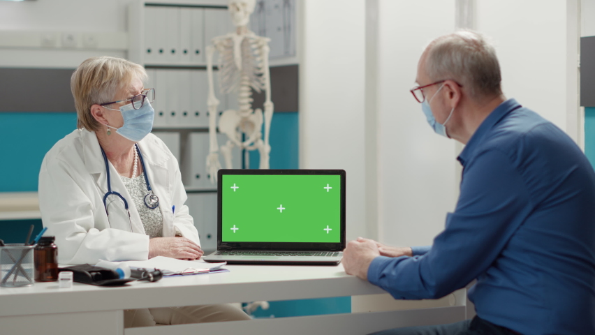 General practitioner showing laptop with greenscreen to retired patient with face mask at appointment. Blank chroma key background with isolated mockup template and copyspace. Tripod shot. | Shutterstock HD Video #1091797843