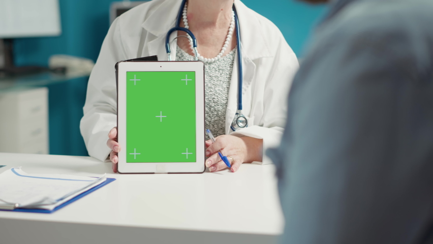General practitioner showing greenscreen on digital tablet in medical cabinet. Female medic holding device with isolated chromakey template and blank mockup copyspace on background. | Shutterstock HD Video #1091797845