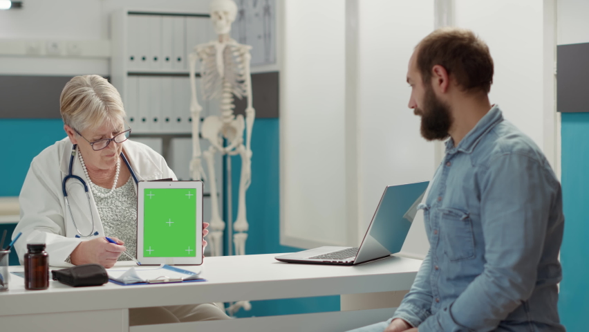 Physician and patient analyzing digital tablet with greenscreen in medical office. Man and medic using blank copyspace mockup with isolated chromakey background and template. Tripod shot. | Shutterstock HD Video #1091797851