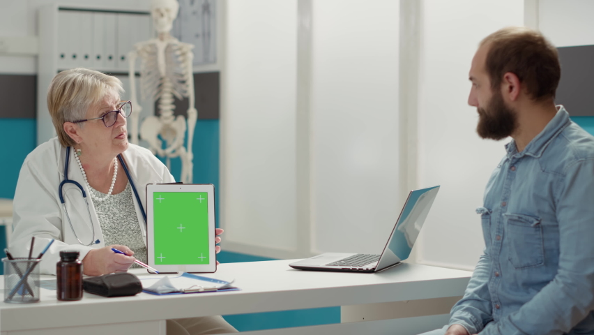 Doctor vertically holding greenscreen on digital tablet in cabinet. People at checkup visit looking at mockup template with isolated chromakey background and blank copyspace on display. | Shutterstock HD Video #1091797865