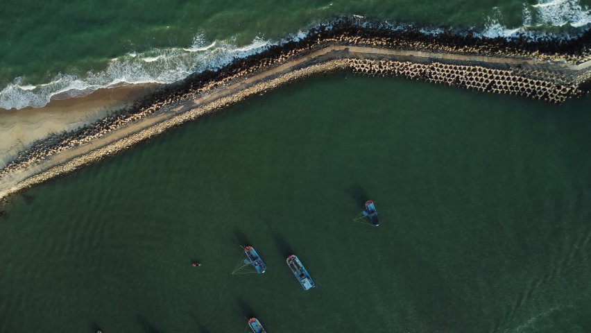 Fishing vessels fishing behind protective wall from powerful ocean waves, top down