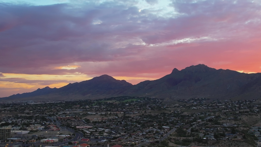 Aerial Drone Shot Of Franklin Mountains Seen From West El Paso Texas During Beautiful Colorful Sunrise With Large Rainbow Clouds In The Background. Camera Flying Down Over City Neighborhood Buildings.