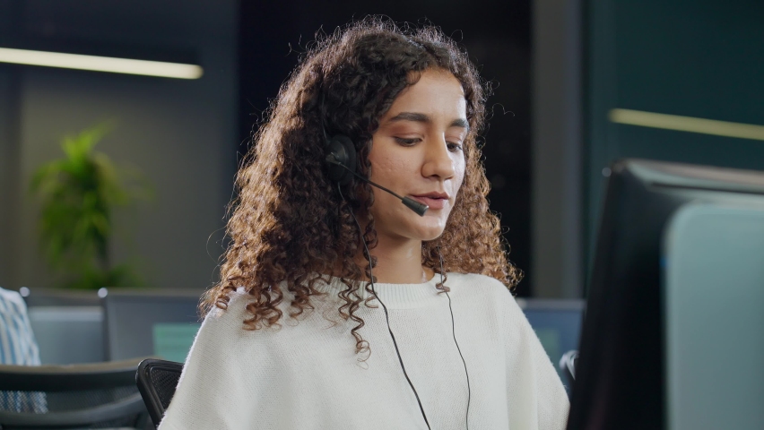 A modern attractive smiling young Indian Asian call center or customer care support curly haired female or woman employee in headset mic busy talking or interacting with client in a corporate office. | Shutterstock HD Video #1091806251