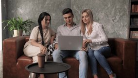 Guy and two girls sit on sofa with laptop making video call greeting friend. Online conversetion.Social distance at home.