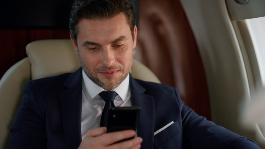 Successful man looking smartphone at airplane window. Delighted businessman rest checking social media reading news on business trip in suit. Confident financial analyst enjoying scrolling cell phone | Shutterstock HD Video #1091820915
