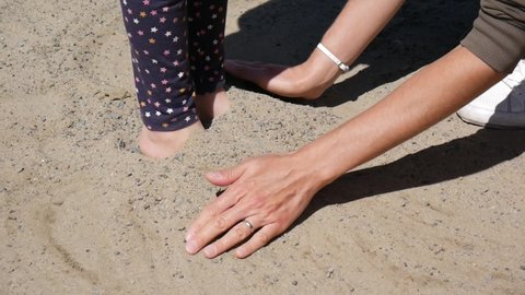 Close-up of mother's hands digging her daughter's feet into the sand and then she jumps out of it