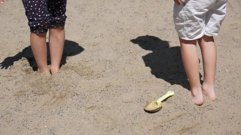 Close-up of a girl's and a boy's feet buried in the sand and they jumping out of it