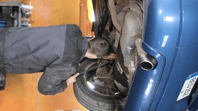 Vertical video, a mechanic inspects the car's running system. Worker in uniform. Defective car