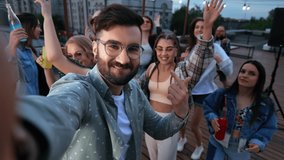 Closeup fashion hipster man blogger shooting POV selfie photo video with group of dancing fun people at dancefloor roof party. Overjoyed friends dance movement together relaxing summer outdoor disco