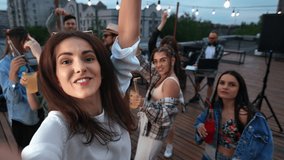 Female celebrity influencer posing POV selfie at summer outdoor night roof party with dancing friends crowd. Happy blogger vlogger shoot photo video online broadcasting social networks at nightclub