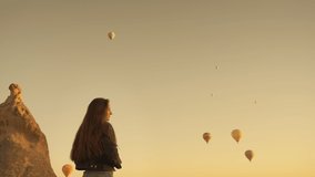 Side view of young female brunette traveler taking video of hot air balloons floating in sky in early morning in Cappadocia. High quality 4k footage