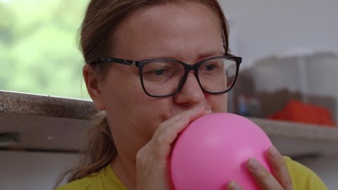 close-up girl glasses inflates a pink balloon to arrange a surprise for the holiday