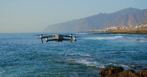 Remote controlled unrecognizible drone flies over water. High resolution video camera flying above the sea against a sunset sky.