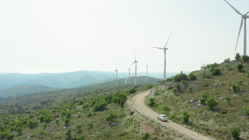 Aerial view of windmills in the mountains and car traveling. Landscape nature and a source of clean energy from the air, people and nature. Royalty-Free Stock Footage #1091831981