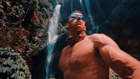 Muscular man travel in tropical rainforest jungle and enjoy beautiful waterfall on nature background 4K