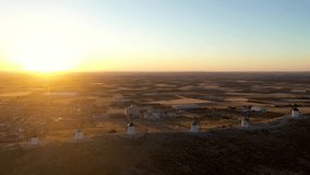 Aerial view of Windmill of Consuegra. Underexposed video at sunrise.  Sun in front of the camera at sunrise. Beautiful Warm colours. Drone pan right and sun moving from one windmill to another