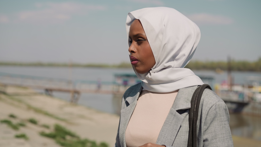 Sorrowing African-American woman with headscarf stands on embankment closeup slow motion. Unhappy Muslim lady at riverside. Heartbroken person portrait | Shutterstock HD Video #1091839501