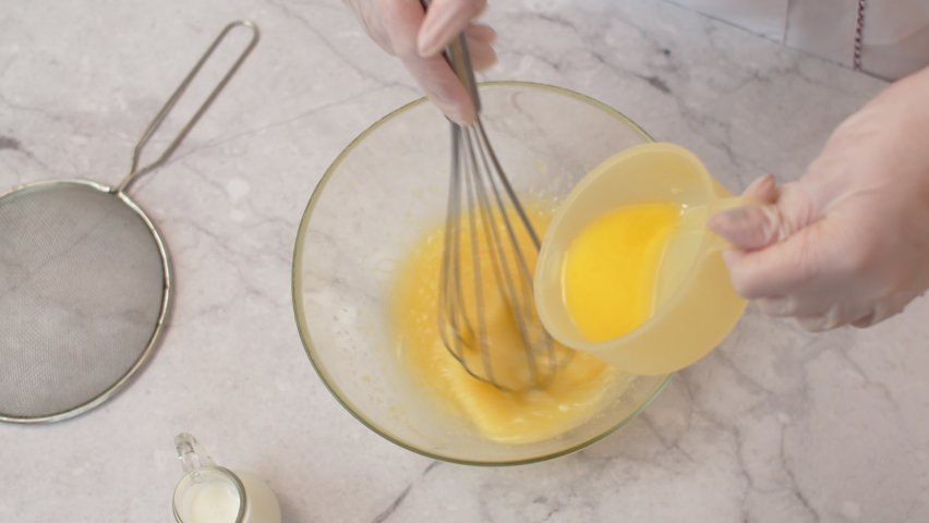 Cook's hands stir beaten eggs with a whisk, pouring oil into bowl, top view. Pastry chef whipping eggs for cream, close-up. Chef prepares the cream by whipping with a whisk, mixing the ingredients | Shutterstock HD Video #1091839525