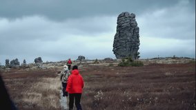 Three people go to a high mountain of stones. CLIP Stone ridge in the background. autumn steppe