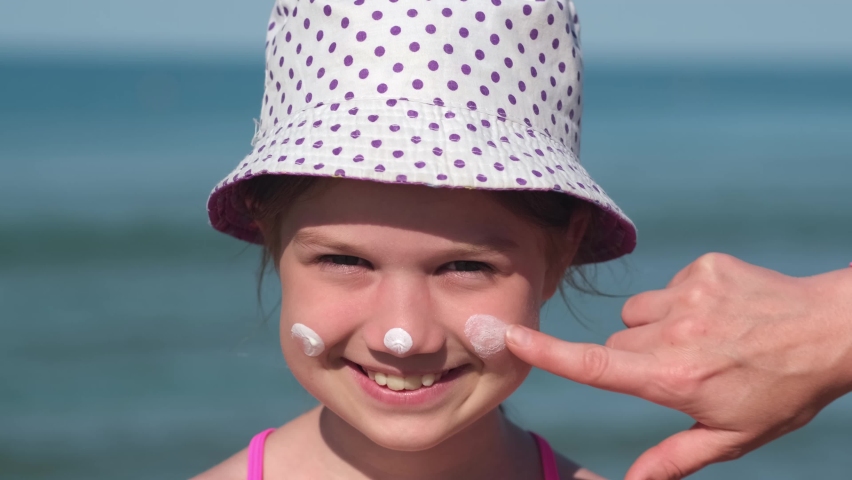 Mother applying protective sunscreen on daughter nose at beach on summer holiday vacation. Woman hand with care putting sun lotion on child face. Happy little girl with sunblock at sea taking sunbath | Shutterstock HD Video #1091842929