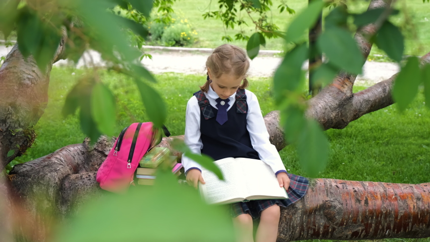 Cute schoolgirl reading a book while sitting on a tree branch. Literature, education and back to school concept | Shutterstock HD Video #1091844305