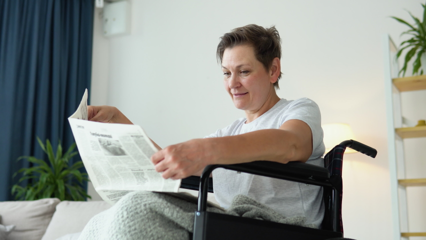 Senior woman sitting in a wheelchair and reading a newspaper at home