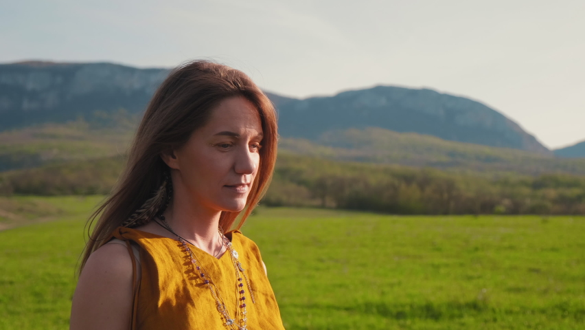 a beautiful girl in boho clothes walks through a green field. Girl run through the green grass at sunset. a woman walks in the field. a woman walks through a very beautiful landscape