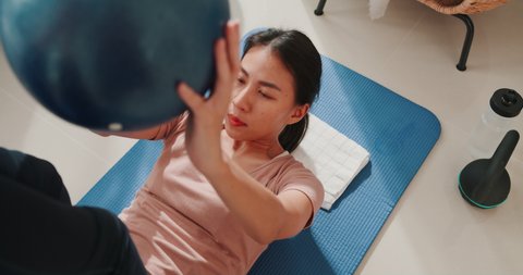 Close up of Young attractive sporty Asia strong woman in sportswear with calm feeling warming up stretching with fitness ball in living room at house. Home quarantine workout and fitness exercise., videoclip de stoc