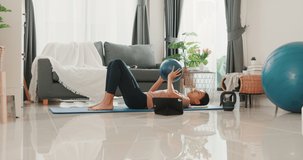 Young attractive Asia woman in sportswear watching fitness online video on tablet with fitness ball in living room at house. Home quarantine workout and fitness exercise without the gym.