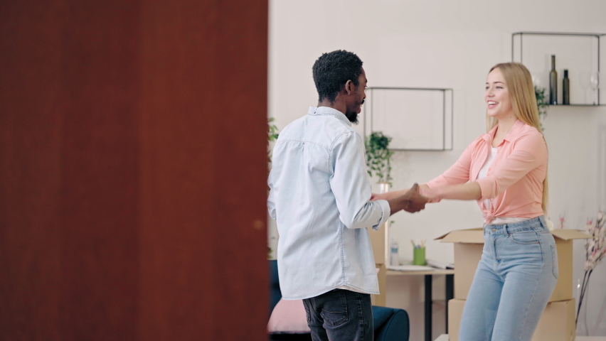 Cheerful interracial couple dancing, celebrating moving into new apartment
