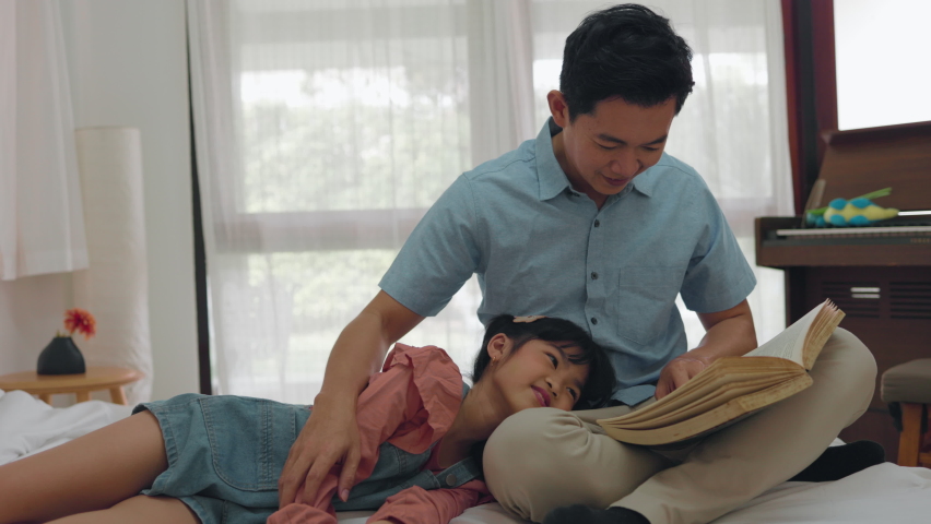 Happy family Asian mature dad reads fairy tales to cute little daughter in bed at home. father's day concept | Shutterstock HD Video #1091860273