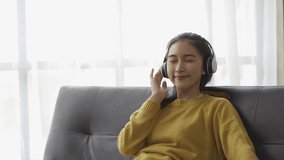 View of Asian woman wearing headphones listening to music on a sopa at home having fun.video 4k