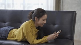 View of Asian woman using smartphone to chat with friends online on Sopa at home, 4k video.