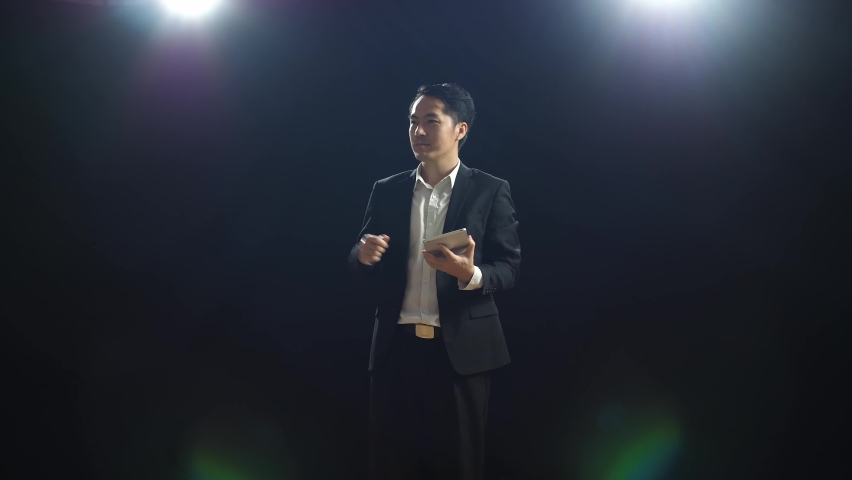 Asian Speaker Man In Business Suit Holding And Pointing Green Screen Tablet While Speaking In The Black Screen Studio
