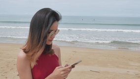 asian woman texting mobile phone while walking on the white sand beach in summer vacation holiday time. workcation concept.