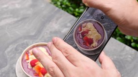 Man, influencer, blogger shoot on phone camera breakfast, restaurant food. Male hands making photo, picture, shots for social media of healthy fruit and berries smoothie bowl on smartphone. Close-up.