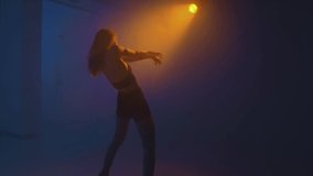 Beautiful graceful girl dancing in colorful studio light in smoke at night. Modern dance, slow motion, handheld video