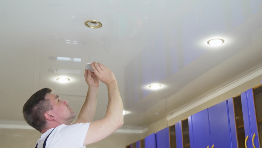 A male electrician changes the light bulbs in the spotlight ceiling lamp. men's household duties. care of electrical appliances at home. | Shutterstock HD Video #1091879395