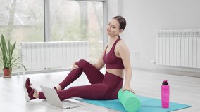 online fitness. a woman in a burgundy tracksuit with laptop on a mat in a gym. Record video and online lessons for sports. clothes and shoes for gymnastics. professional trainer.