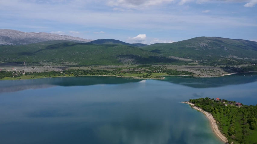 A lake in northern Croatia surrounded by greenery and mountains on a bright partly cloudy day. This lake lies very close to the Bosnian border.