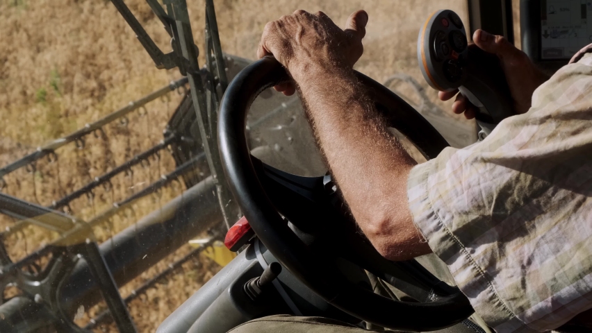 Farmer-driver man's hands on the wheel of the combine. Harvesting in an agricultural field. View from the inside. The tractor driver turns the wheel of an agricultural machine. 
 | Shutterstock HD Video #1091890435