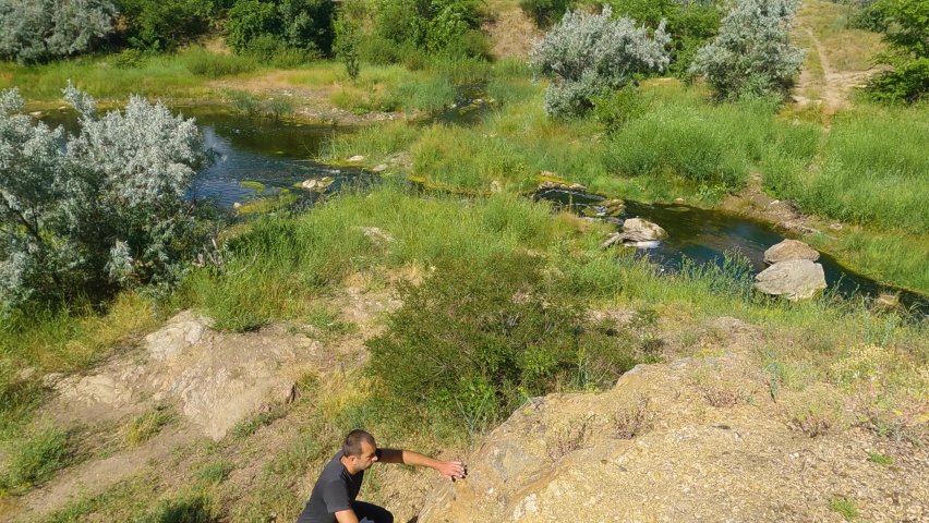 The man in the sneakers is climbing up the rocks. Near of the river. Slow motion