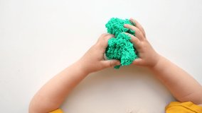 Baby Hands Playing with textured slime with bubbles, stretching the gooey substance on white background. Little child hand holding green shining slime toy squeezing it to the sides. Top View 4K video