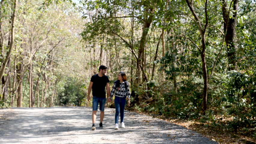 Happy love couple take photo and selfie during camping and relax in forest hiking trip, beautiful Asian woman and caucasian man happiness spend time tpgether, sunset liesure romantic moment
