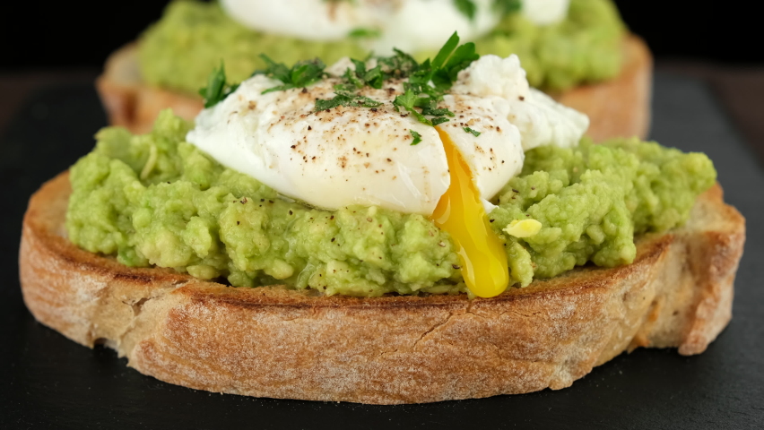 Cutting poached egg with runny egg yolk over bread toast with mashed avocado spread. Avocado toast with poached egg close up. Healthy breakfast or lunch food. | Shutterstock HD Video #1091901373