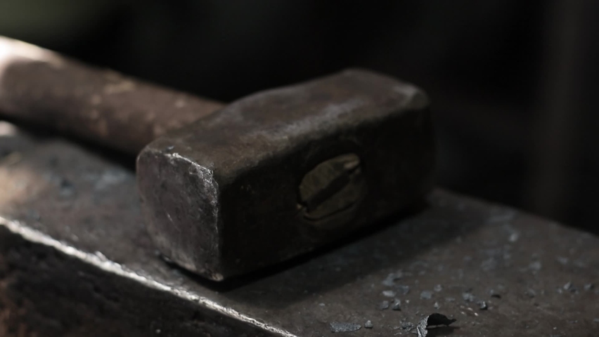 Professional male blacksmith forming red hot metal on an anvil in interior blacksmith workshop.