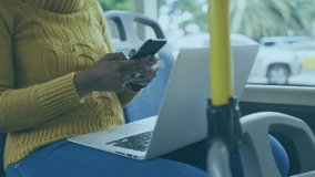 Animation of virus cells over african american woman wearing face mask, using smartphone in bus. Global covid 19 pandemic concept digitally generated video.