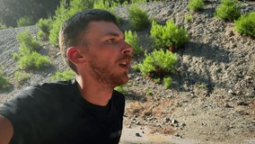 Selfie portrait of young sportive man trail runner running on rocky mountain ridge at sunny morning. Active muscular male athlete jogging outdoors and making selfie video. Sport concept