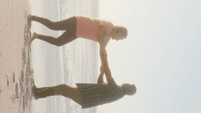 Smiling senior african american couple holding hands and dancing on sunny beach. healthy, active retirement beach holiday.